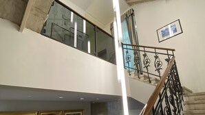 A multi-level interior with a staircase, framed artwork on the walls, and a balcony.