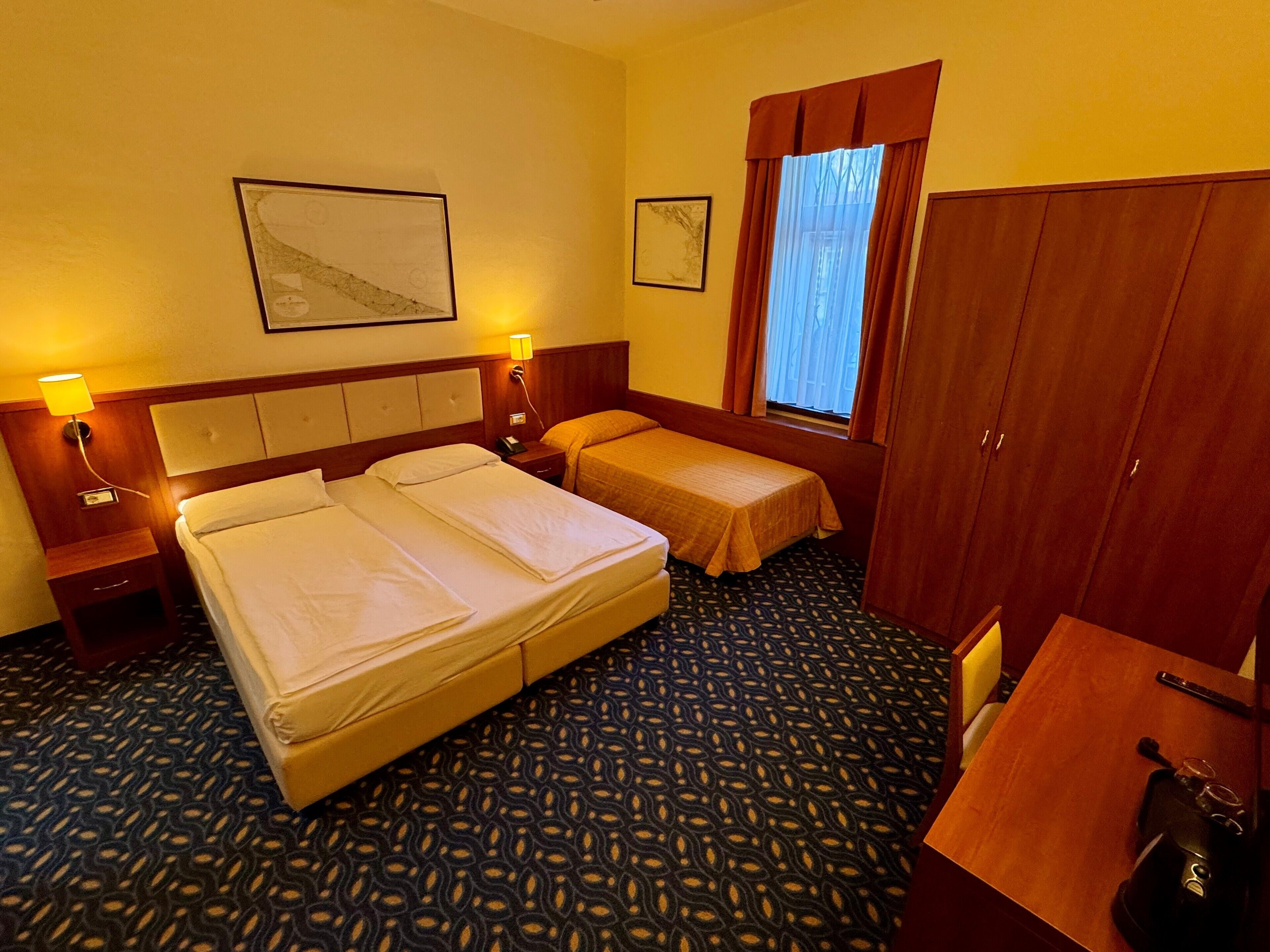 Una habitación de hotel con dos camas, un escritorio, un armario y una ventana con cortinas.