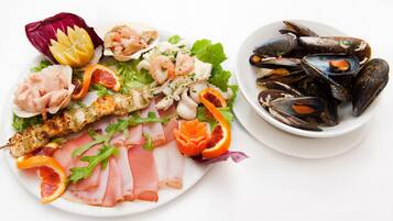 A plate of seafood including mussels, shrimp, and a grilled fish fillet, garnished with citrus slices and herbs.