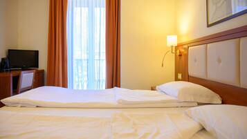 Camera d'albergo con due letti, televisione, scrivania e finestra con tende.