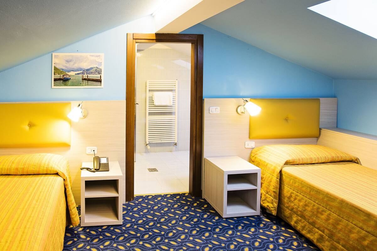 A room with two beds, a small bedside table with a phone, a radiator, and a picture on the wall.