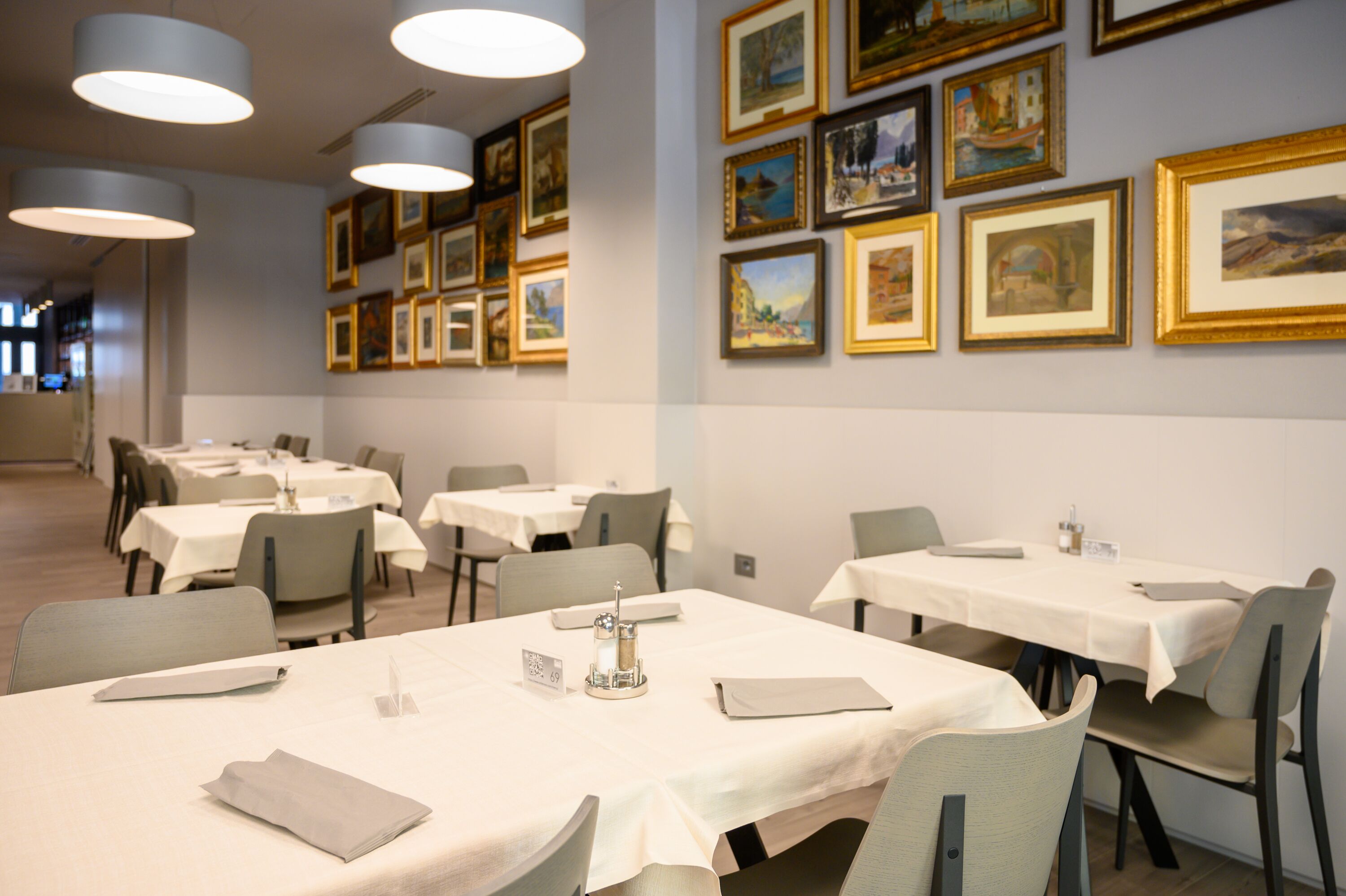 Comedor con mesas dispuestas para el servicio, obras de arte en las paredes y un diseño interior moderno y limpio.