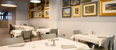 Comedor con mesas dispuestas para el servicio, obras de arte en las paredes y un diseño interior moderno y limpio.