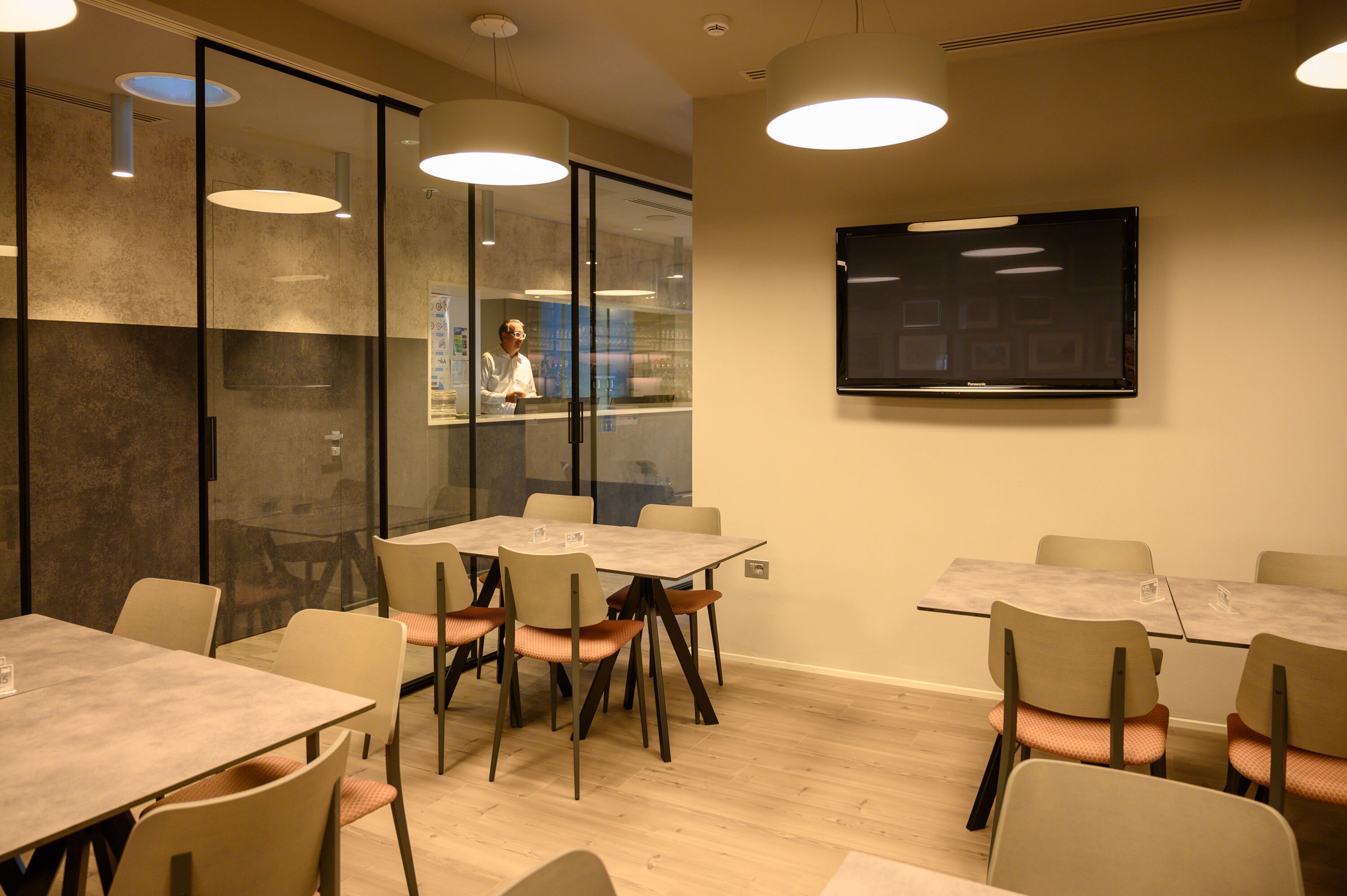 A conference room with glass partitions, a flat-screen TV, and multiple tables and chairs.