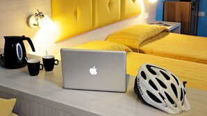 A neatly arranged hotel room with a bed, a desk with a laptop, a helmet, and a coffee maker.