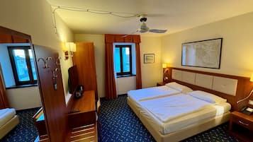 Habitación de hotel con cama, mesitas de noche, escritorio, silla, ventilador de techo y ventana.