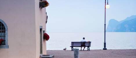 A calm lake with a small boat docked near a building with flower boxes and a bench by the water.