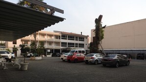 Un estacionamiento con varios autos, un edificio de varios pisos y un pasillo cubierto.