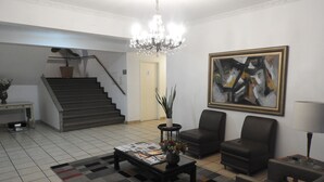 Amplio salón con escaleras, un candelabro, una mesa de centro con revistas y un cuadro abstracto de gran tamaño.