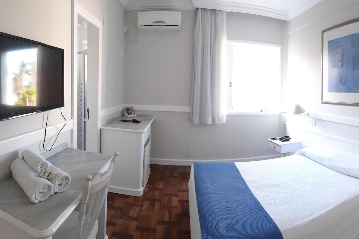 A hotel room with a bed, a desk, a TV, a bathroom, and a window.