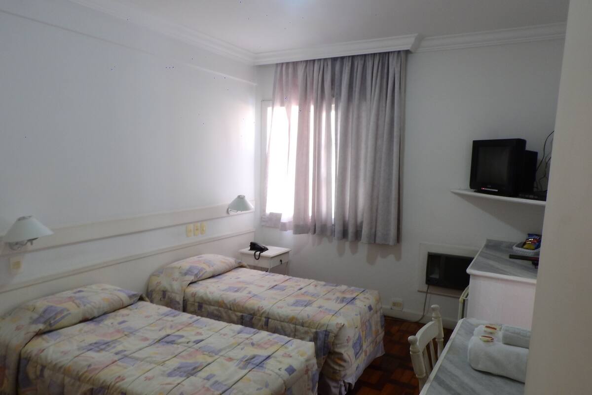 A hotel room with two beds, a desk, a television, and a window with curtains.