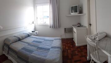 A bedroom with a bed, a TV on a shelf, a desk, and a chair.