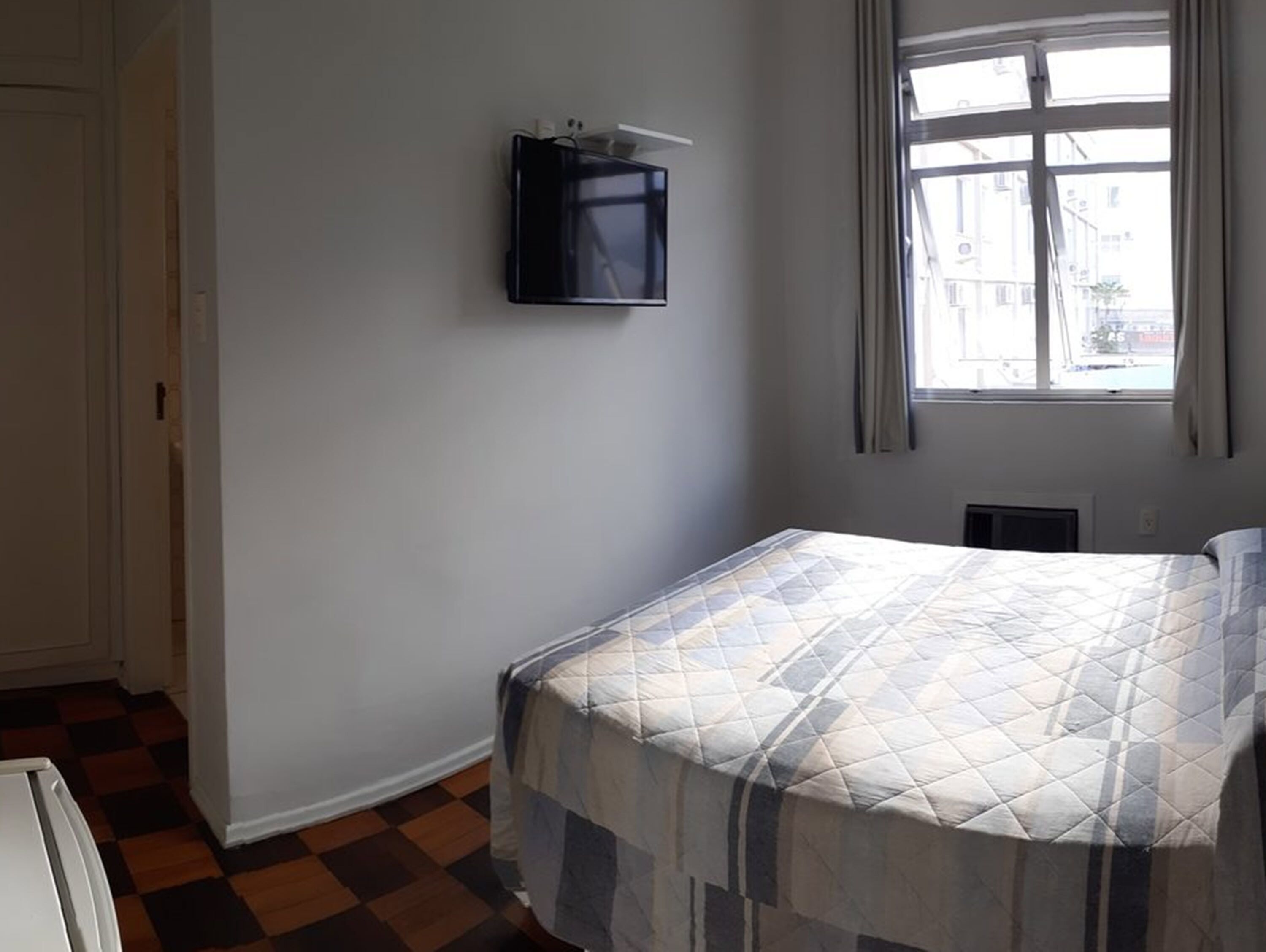 A bedroom with a bed, a television mounted on the wall, and a window with curtains.