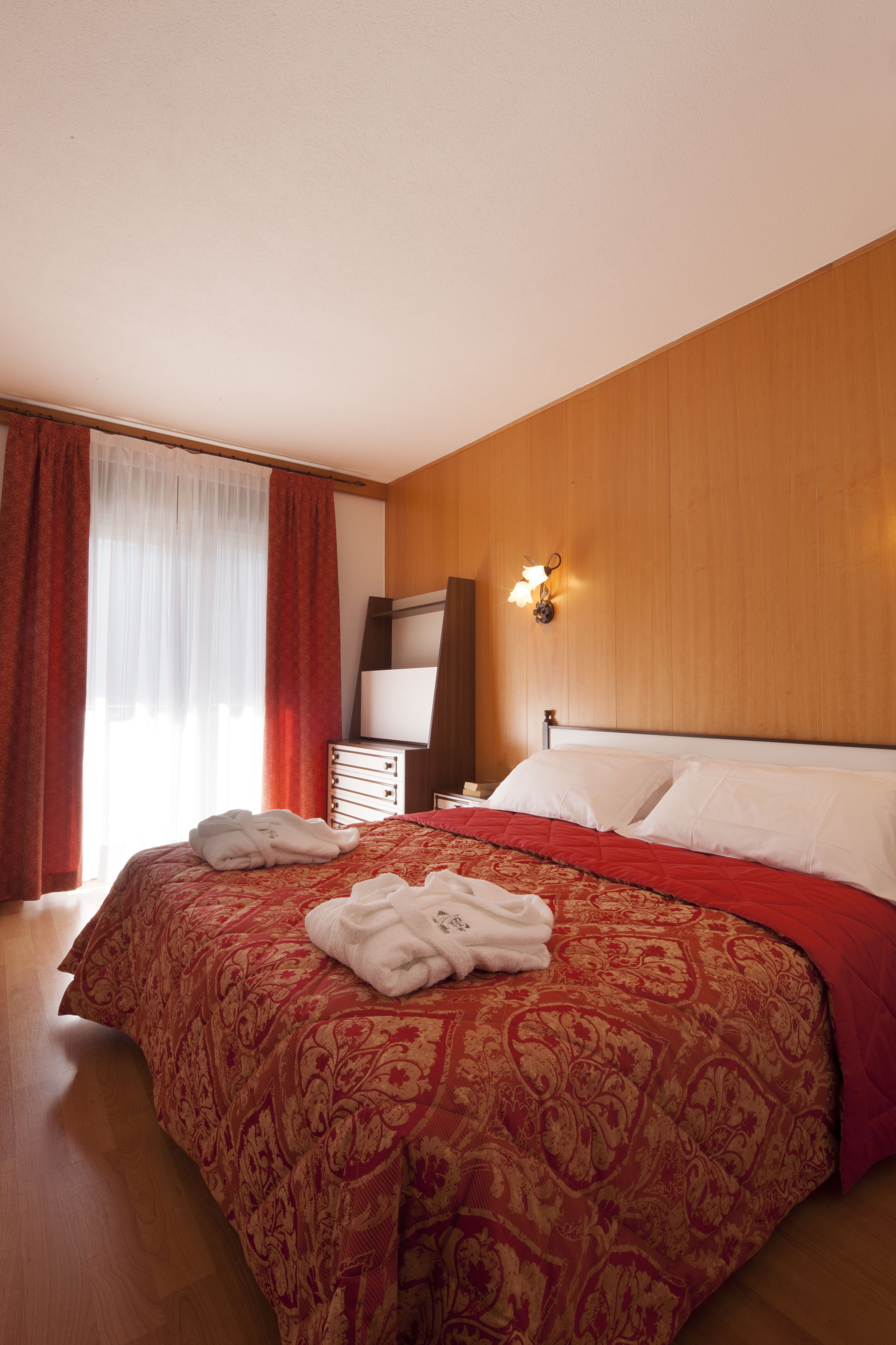Habitación de hotel con una cama grande, paredes de panel de madera, un televisor de pantalla plana y una mesita de noche con lámpara.