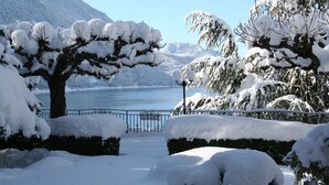 A snow-covered landscape with a lake, trees, and a metal fence. - Miralago (Molveno)