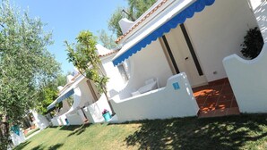 A white building with a blue awning and a tiled roof, surrounded by greenery. - Hotel il Melograno (Mattinata)