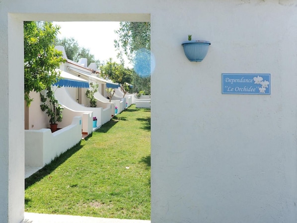 Una hilera de villas blancas con detalles azules, un césped y un cartel que dice 'Dependance 'Le Orchidee'.