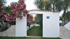 A white building with a tiled roof, a stone wall, and a blue bowl mounted on the wall. - Hotel il Melograno (Mattinata)