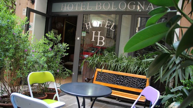 Un área de estar al aire libre con una mesa y sillas frente a un edificio con la leyenda "HOTEL BOLOGNA".