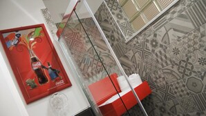Un baño con baldosas estampadas, cabina de ducha de vidrio y un anuncio de Coca-Cola en la pared.