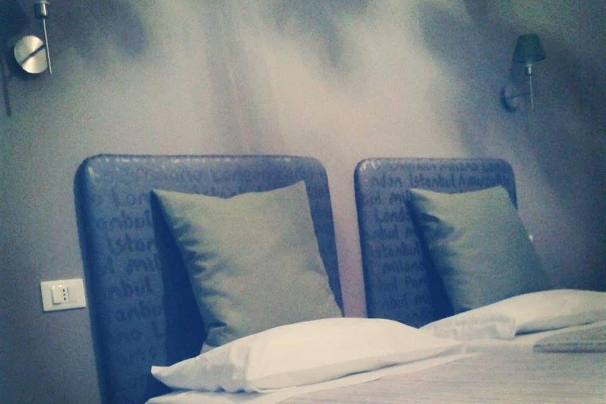 Habitación de hotel con dos camas, cada una con cabecero y almohada, un cesto de basura verde y una lámpara fijada a la pared.