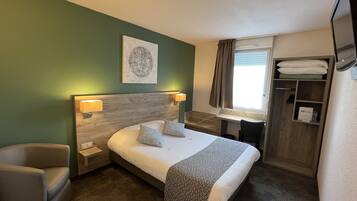 Habitació d'hotel amb un llit, dues làmpades de nit, un capçal de llit, una finestra amb cortines, un armari i una taula petita.