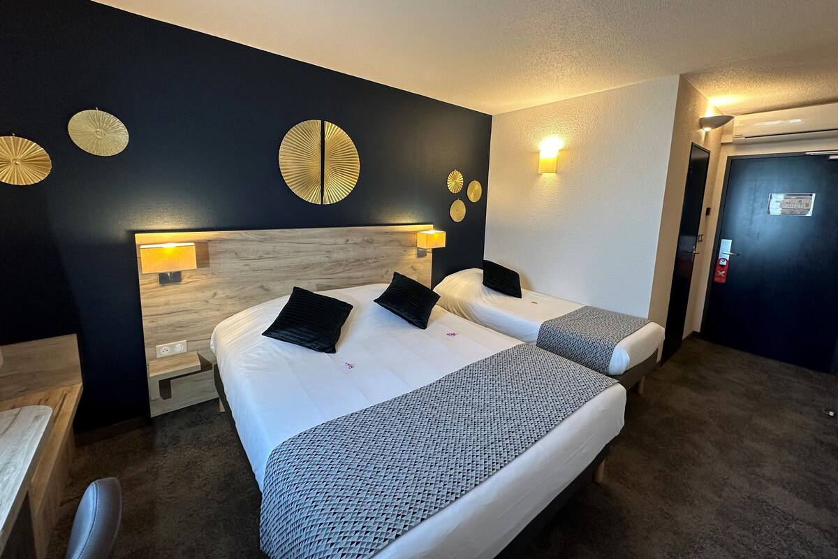 A hotel room with two beds, a wooden headboard, wall-mounted lamps, and a door with a fire alarm.