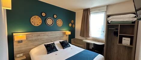 A hotel room with a bed, bedside lamps, a vanity with a mirror, a window with curtains, and a wardrobe.