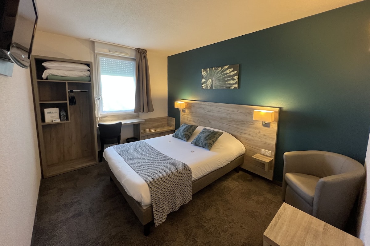 A hotel room with a bed, bedside tables, a desk, a chair, and a wardrobe.