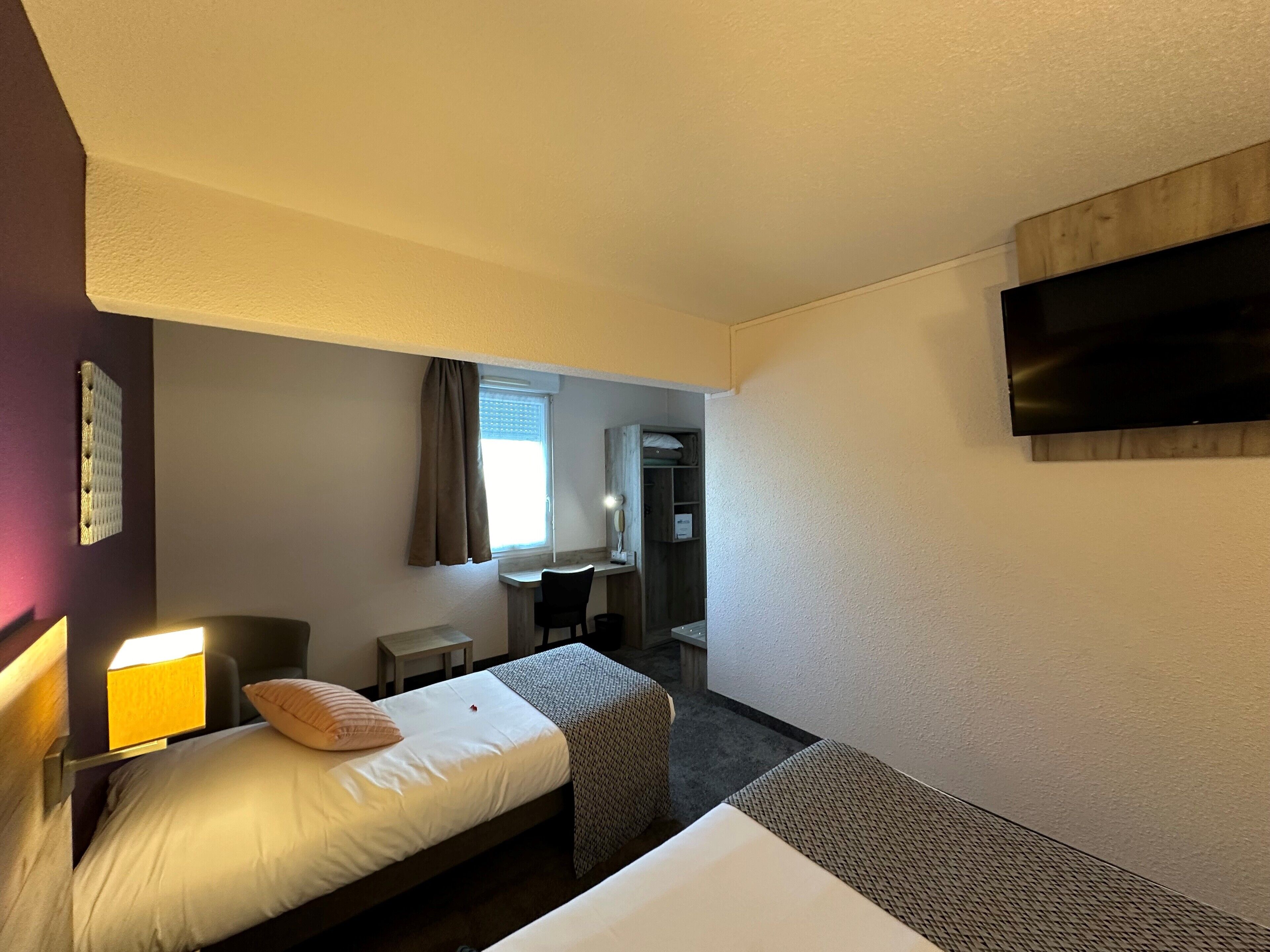A hotel room with a bed, bedside table, lamp, and a TV mounted on the wall.