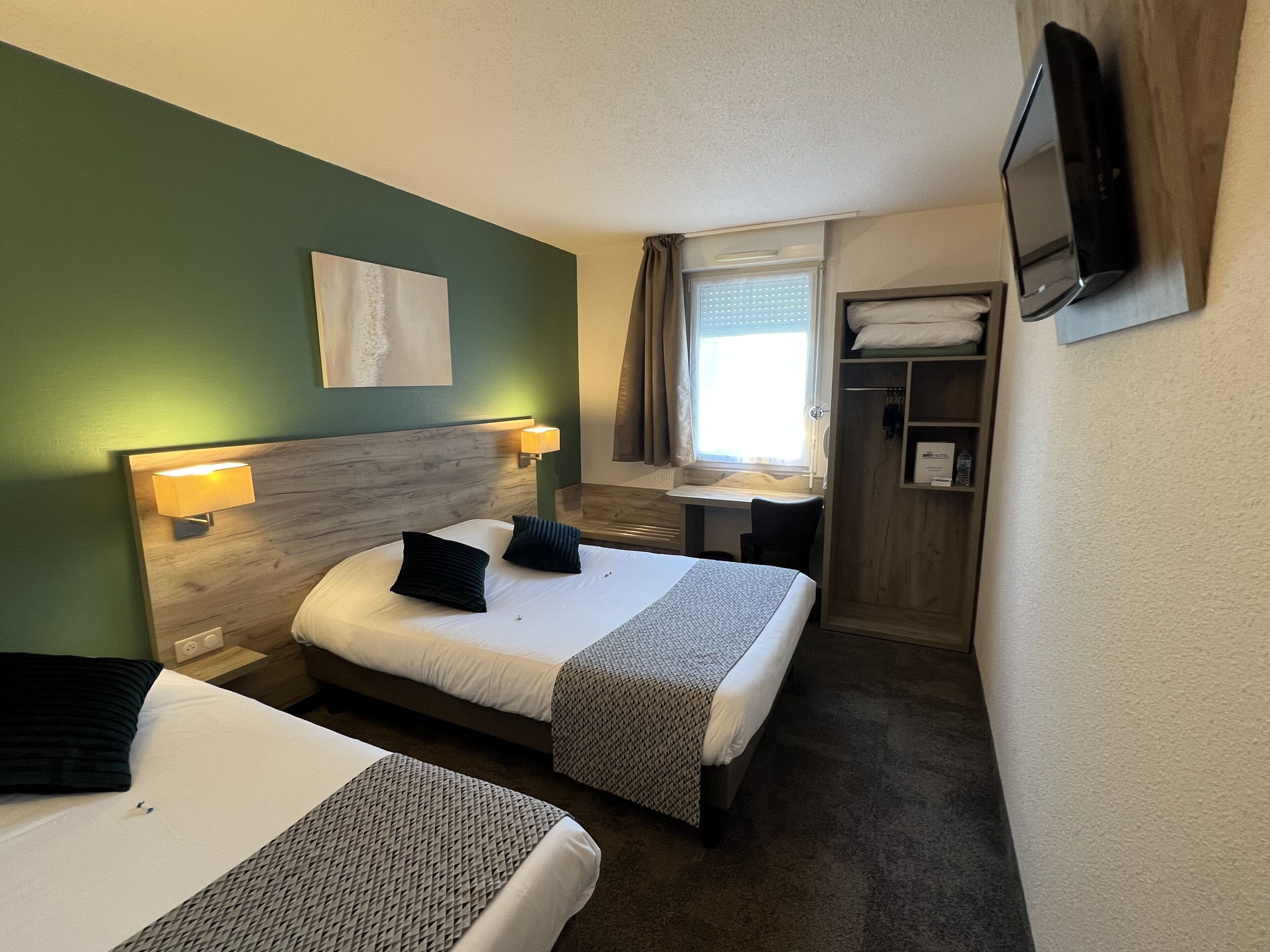 Una habitación de hotel con dos camas, un escritorio, un televisor y un armario.