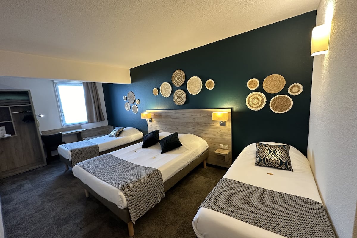 A hotel room with two single beds, a desk, a chair, and a wardrobe.