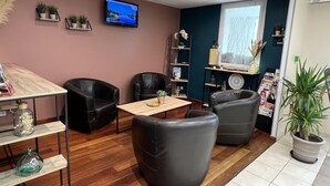 A modern lounge area with leather chairs, a wooden table, and a flat-screen TV on the wall. - Brit Hotel Saumur (Distre)