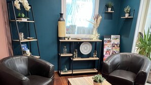 A room with two black leather chairs, a wooden coffee table, a blue wall, a window, and a shelf with magazines and plants. - Brit Hotel Saumur (Distre)