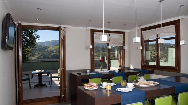 Ein Essbereich mit Blick auf die Berge, ein an der Wand befestigter Fernseher und ein Frühstücksbuffet mit Tellern, Tassen und einer Kaffeemaschine.