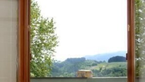 Ein Zimmer mit einer Schiebetür, die auf einen Balkon mit Blick auf Grünflächen und Hügel führt.