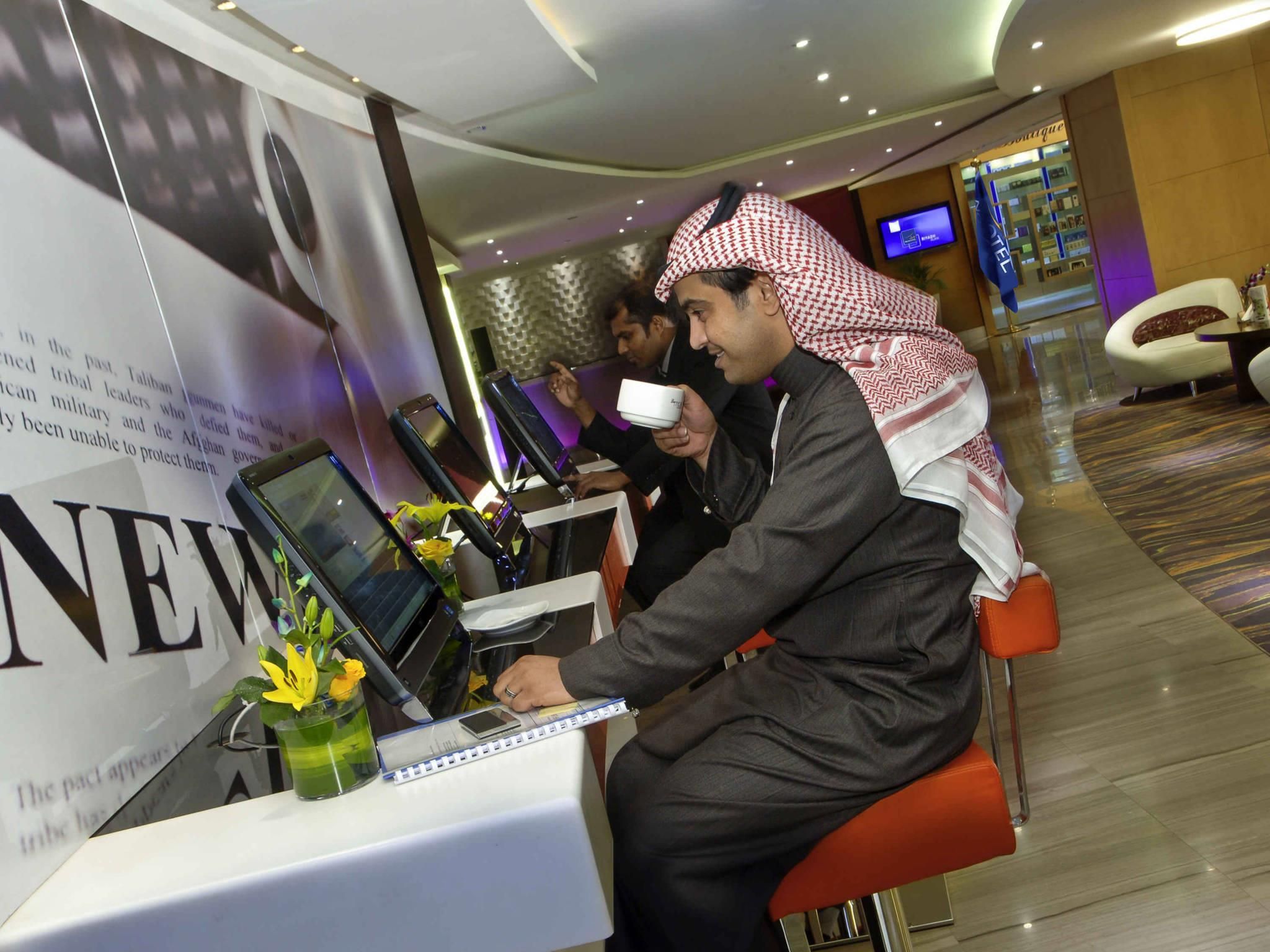 A modern hotel lobby with a reception desk, a digital screen, and a seating area.