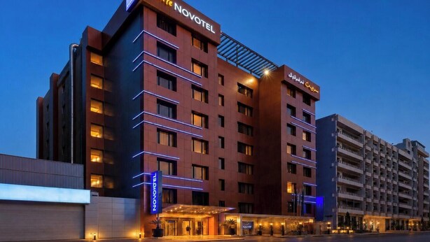 Um hotel moderno com um letreiro chamativo 'Suite Novotel', vários andares e uma entrada bem iluminada.