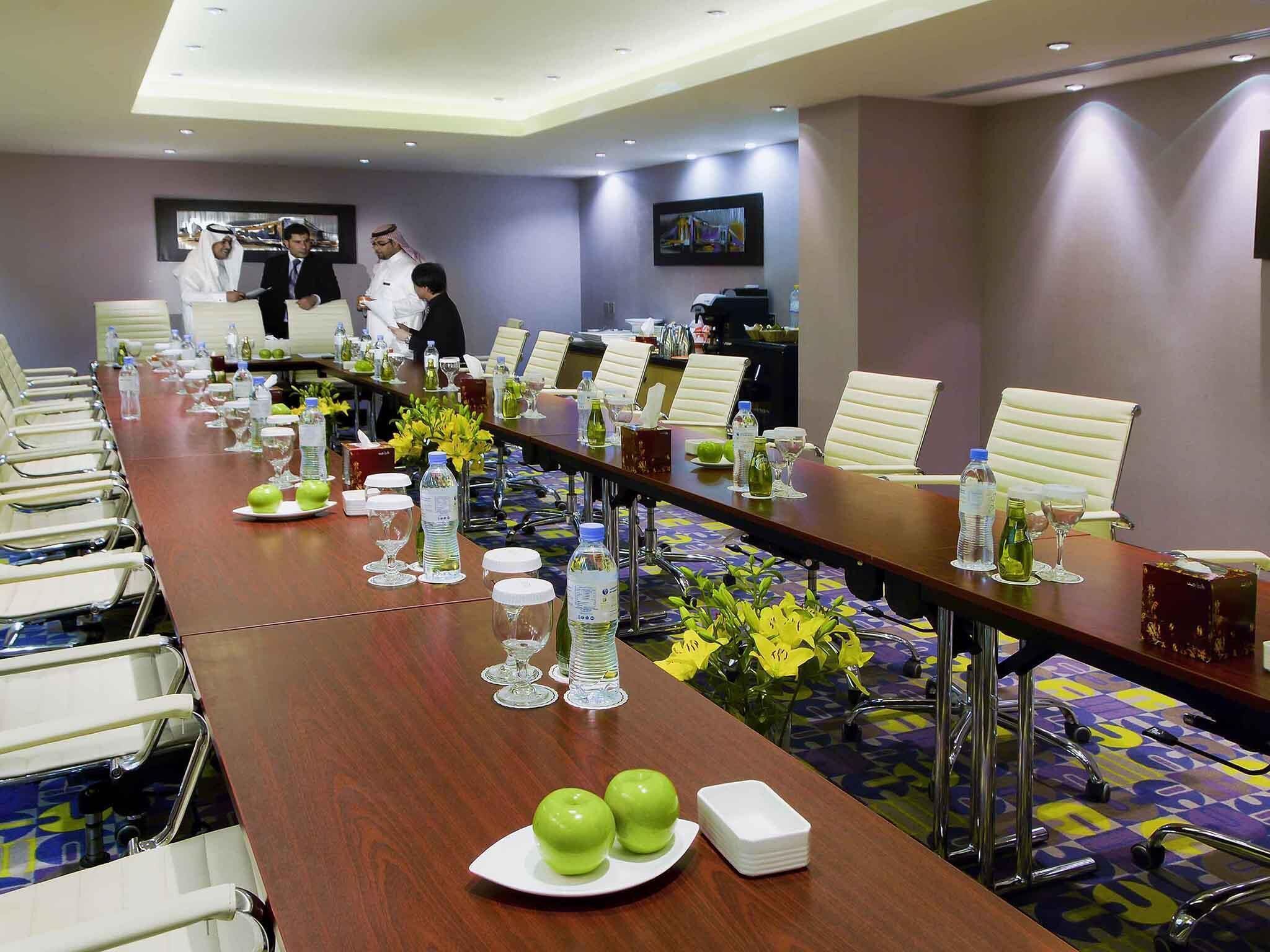 A conference room with a long table, chairs, water bottles, and a television screen.