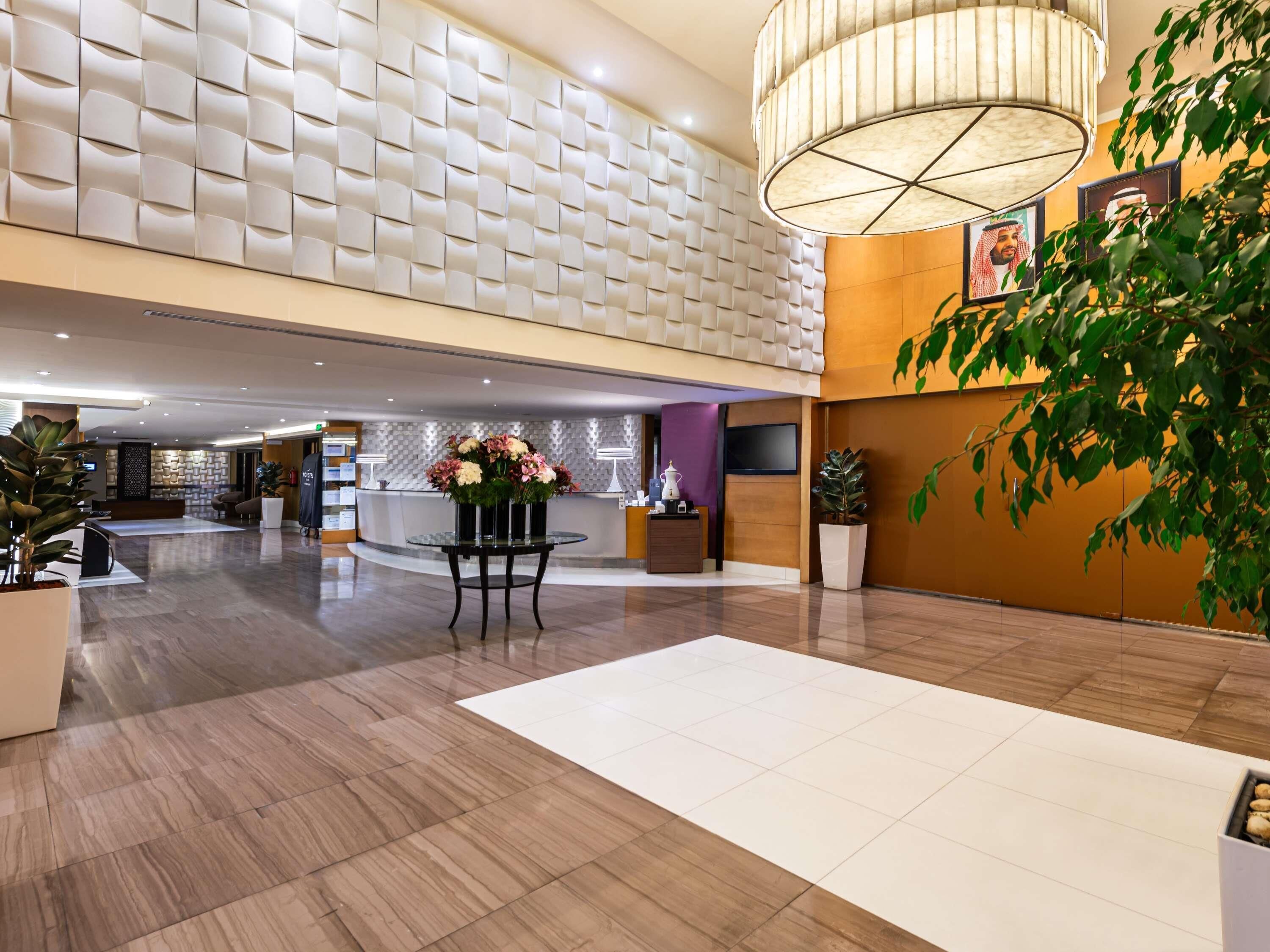A hotel lobby with a reception desk, seating area, and a large plant.