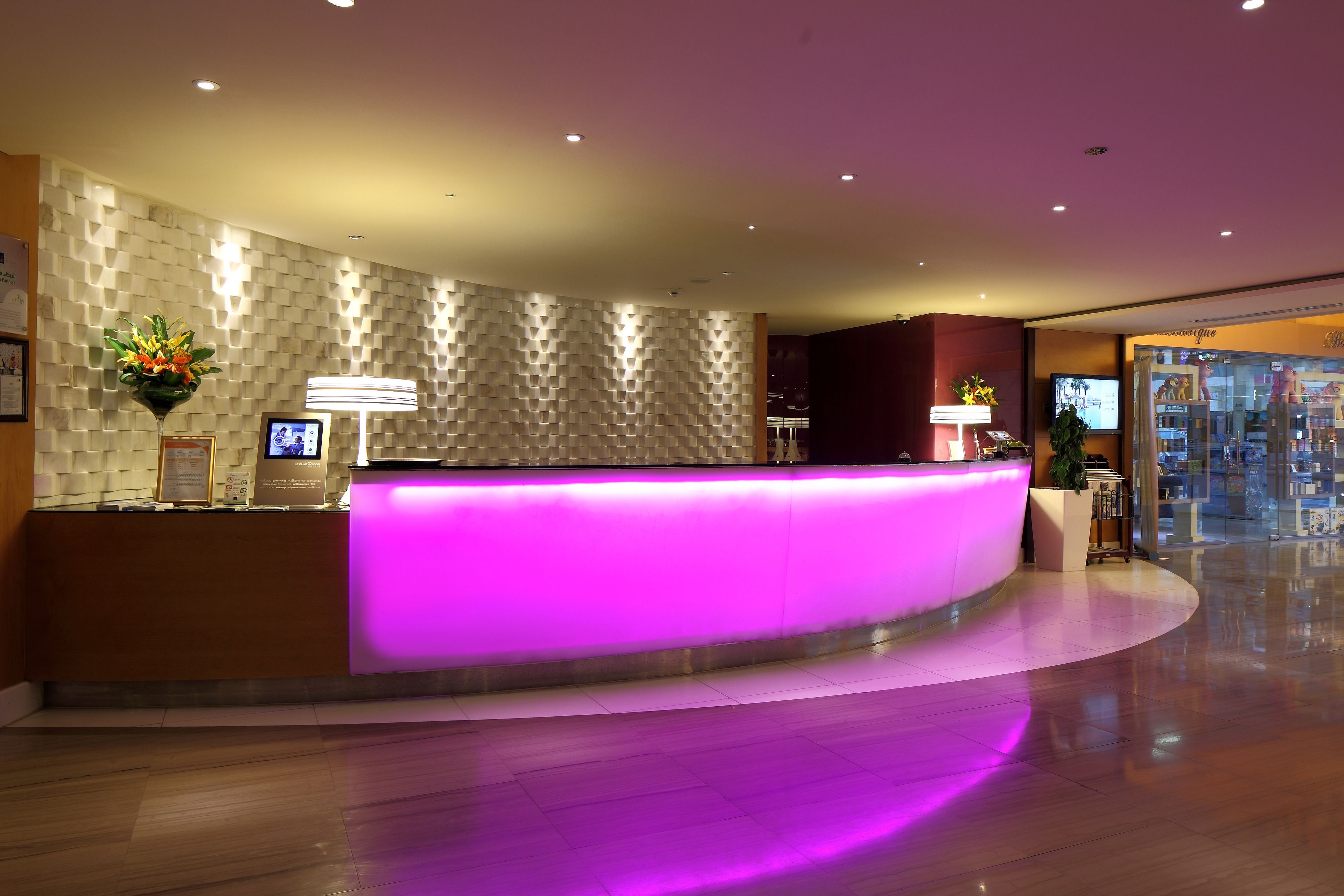 Un'accogliente area reception di un hotel moderno, con una scrivania a forma di arco, uno schermo digitale e un muro con motivo decorativo.