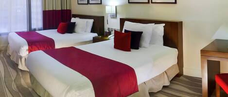 A hotel room with two beds, a bedside table, a lamp, and artwork on the wall.