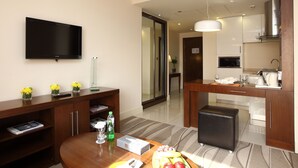 Quarto de hotel moderno com televisão de tela plana, móveis de madeira, área de jantar e uma cozinha compacta.