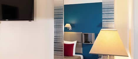 A hotel room with a bed, a TV, a lamp, and a mirror reflecting the room.