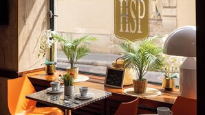 A cafe interior with tables, chairs, potted plants, and a chalkboard sign. - Hotel Saint Pierre (Paris)