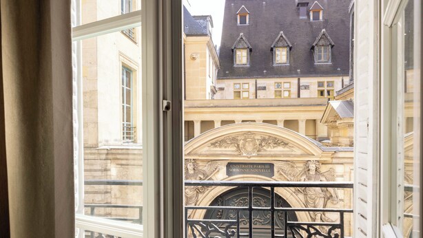 A view through a window of a building with ornate iron gates and a plaque reading "UNIVERSITE PAYS L'ORIENT." - Hotel Saint Pierre (Paris)