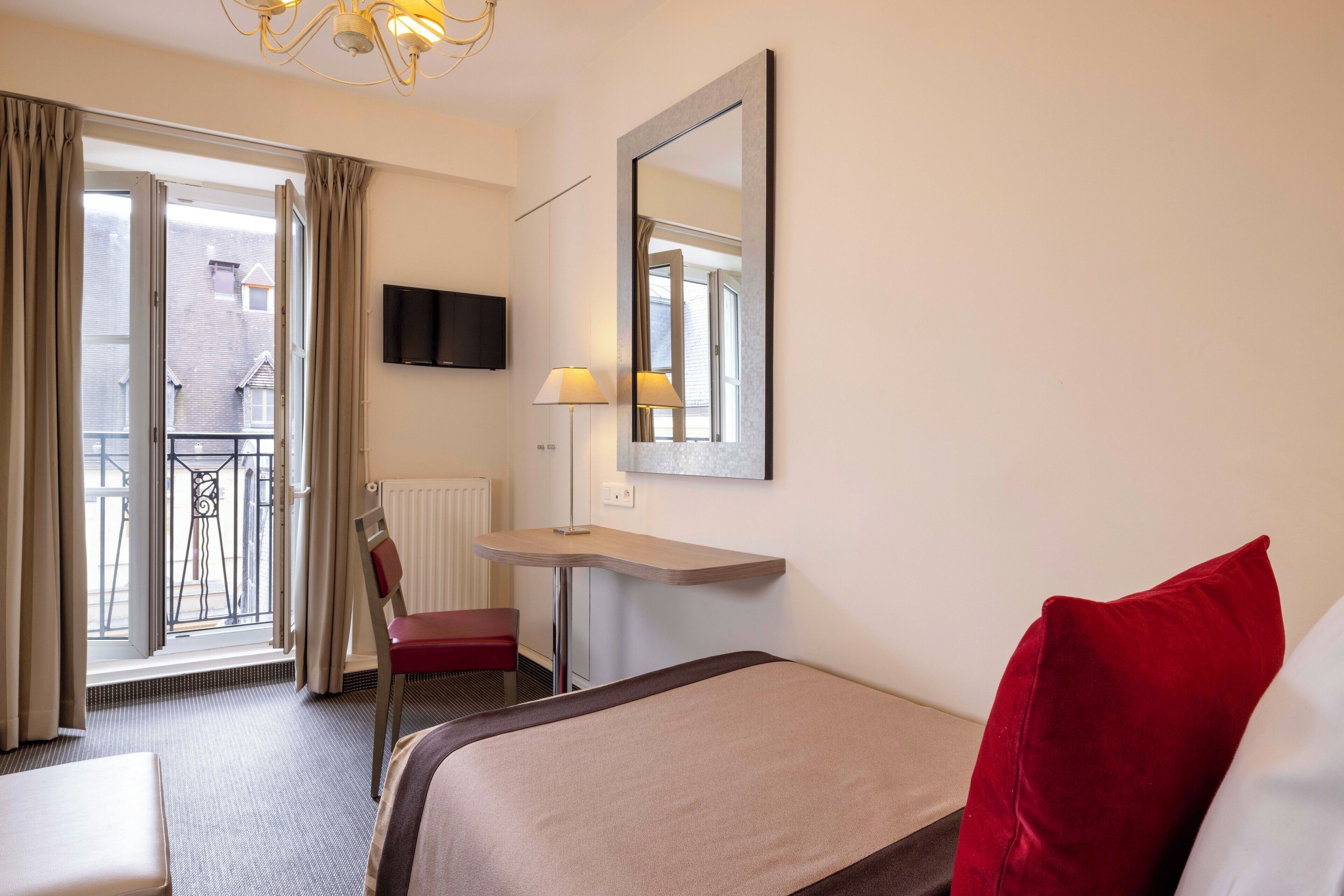 A hotel room with a bed, a desk, a chair, a TV, and a balcony with curtains.