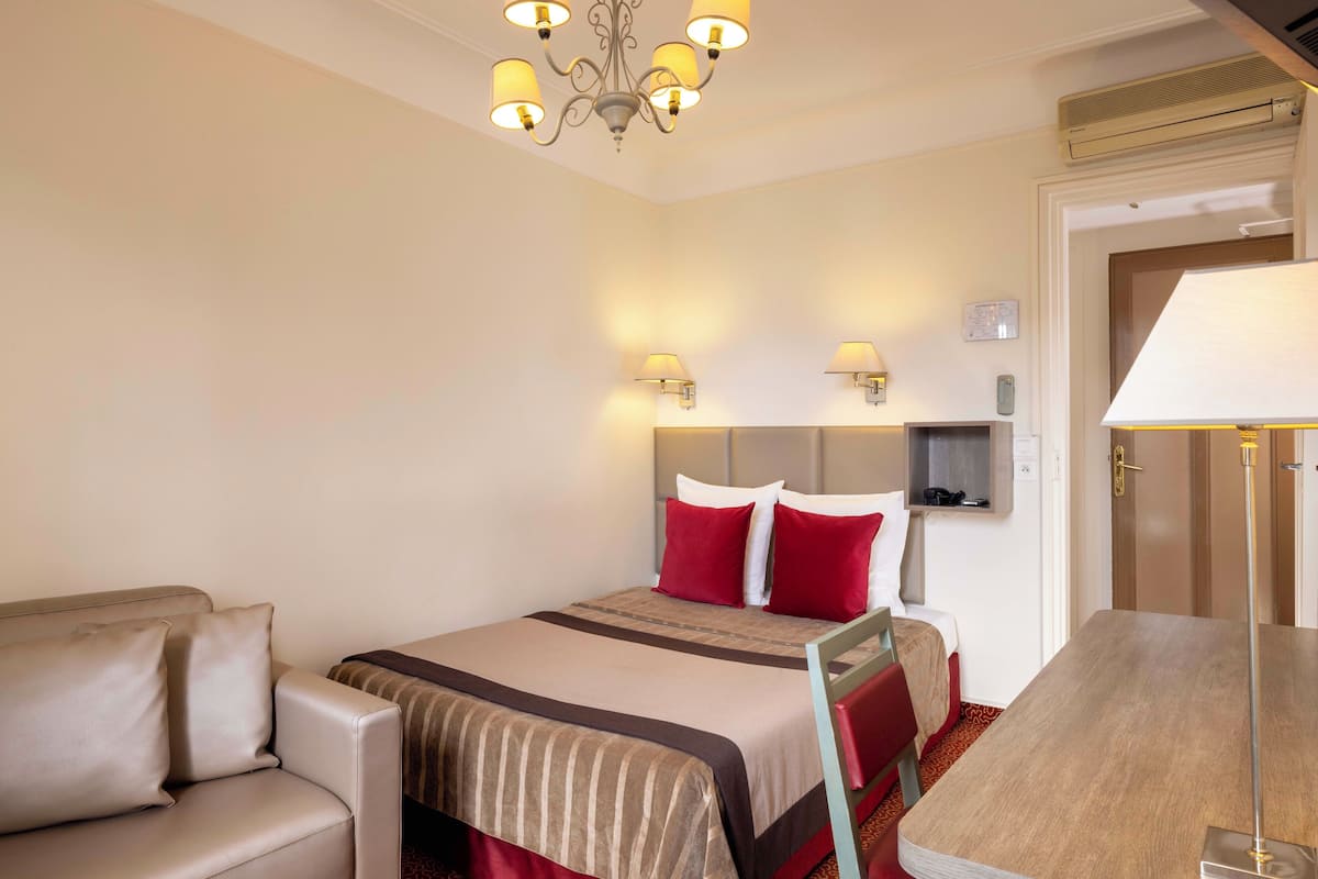 A hotel room with a bed, a sofa, a table, and a chandelier.