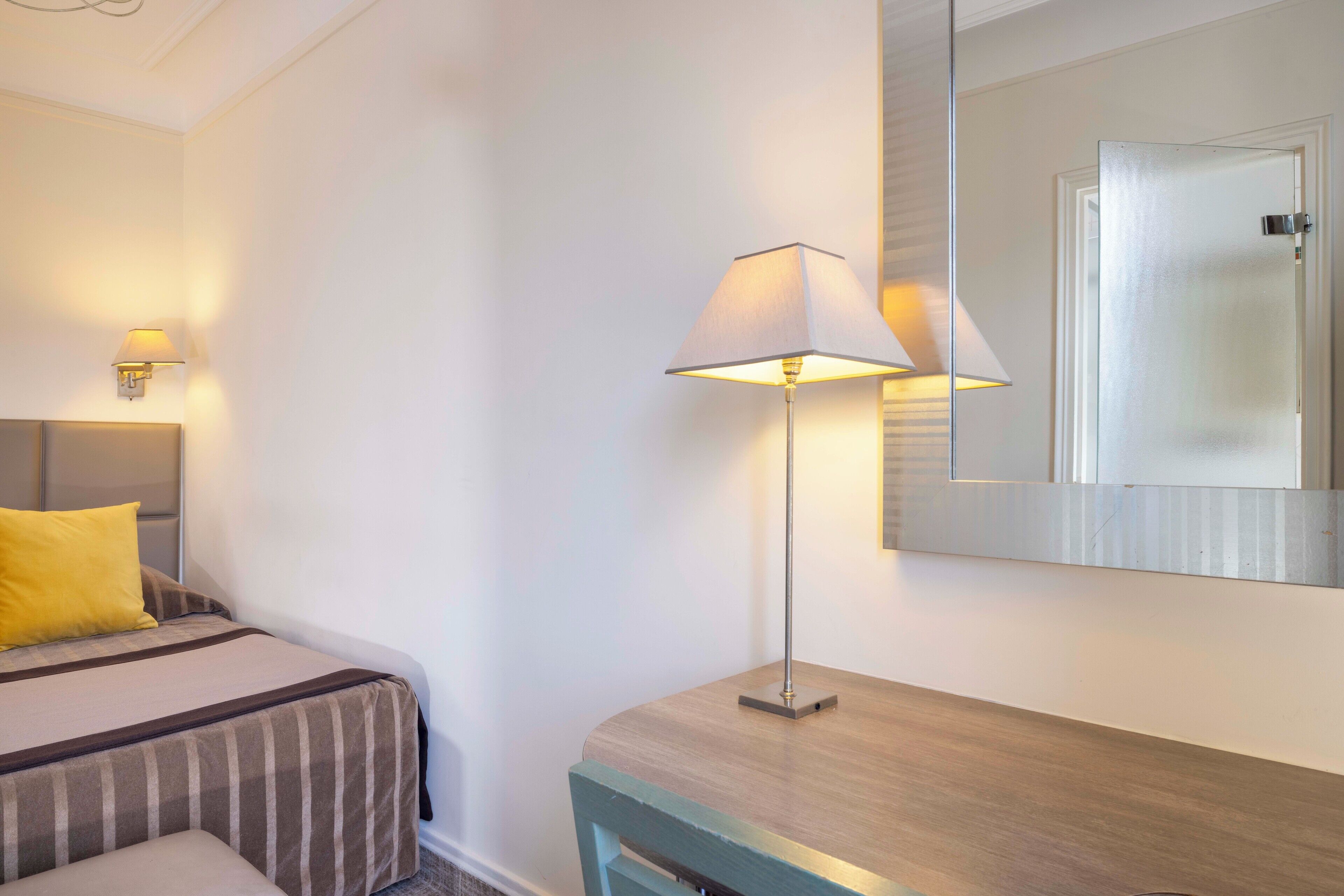 A hotel room with a bed, a bedside lamp, a mirror, and a wooden nightstand.