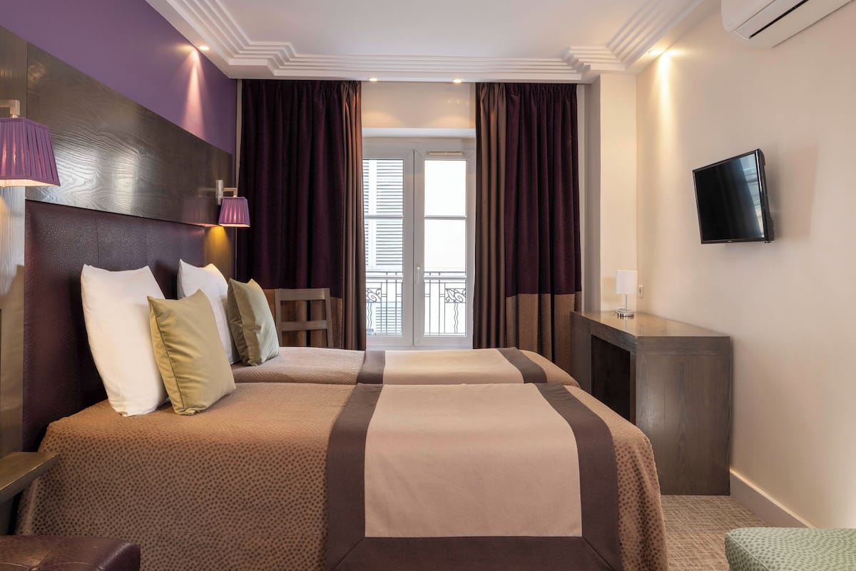 A hotel room with a large bed, a desk, a TV, and a balcony with curtains.